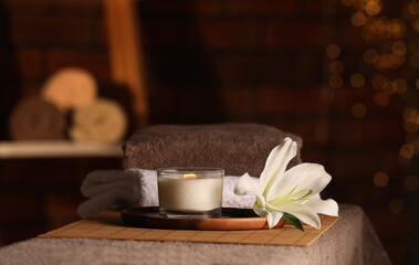 Spa composition with burning candle, lily flower and towels on massage table in wellness center, space for text