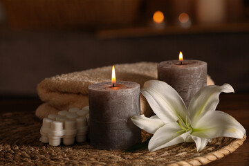 Spa composition with burning candles, lily flower and towels on wooden table in wellness center