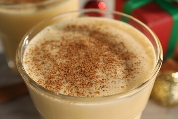 Tasty eggnog with cinnamon in glass on table, closeup
