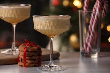 Tasty eggnog, cookies and candy canes on white marble table against blurred festive lights, closeup
