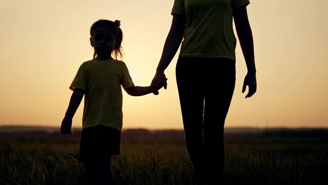 Happy family concept.Mom with baby is walk on grass in park.Mother with boy in field at sunset. Girl holds child by hand.Active lifestyle concept.Happy girl holds his mother by hand and walk on grass.