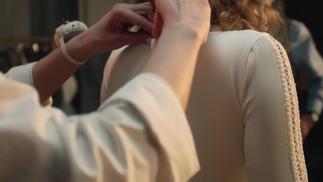 Close-up shot of tailor zipping up wedding dress on woman in front of mirror. Bride on fitting wedding dress in luxury designer atelier or wedding salon. Concept of fashion, handmade and couturier.