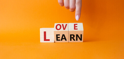 Love and Learn symbol. Businessman hand points at turned wooden cubes with words Learn and Love. Beautiful orange background. Lifestyle and Love and Learn concept. Copy space.