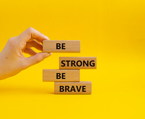 Be strong be brave symbol. Concept words Be strong be brave on wooden blocks. Beautiful yellow background. Businessman hand. Business concept. Copy space.