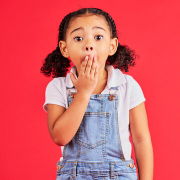 Shocked kid, portrait and hand on mouth in secret, oops and mistake facial expression on isolated red background. Child, little girl and surprised face in gossip, news or emoji at studio announcement