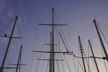 The masts of the ships and yachts in the marina are towards the horizon, with a view of nature in the background.