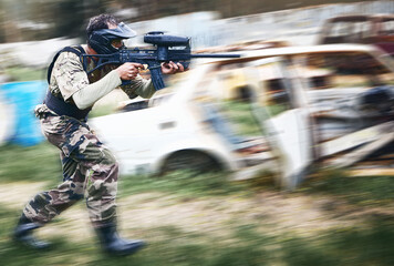 Paintball, aim and man with a gun for a game with blur motion at an outdoor arena or field. Challenge, competition and male soldier with a camouflage military outfit shooting a rifle on a battlefield