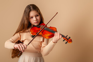 Portrait of a girl with a violin and a bow in her hands on a plain beige background. Music concept