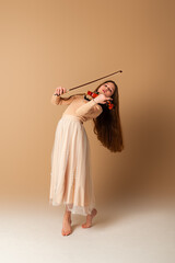 Portrait of a girl with a violin and a bow in her hands on a plain beige background. Music concept