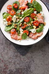 French salad Aveyronnaise with bacon, walnuts, and Roquefort cheese and other ingredients closeup on the plate on the table. Vertical top view from above