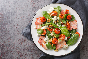 Warm french salad with bacon, spinach, roquefort cheese, walnuts, tomatoes, basil and garlic close-up in a plate on the table. Horizontal top view from above