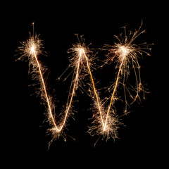 Sparkling burning creative letter W isolated on black background. Beautiful glowing golden overlay object for design holiday greeting card. Creative lettering W written with burning sparklers