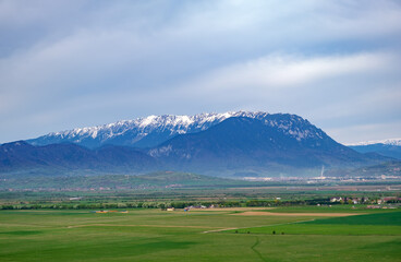 Beautiful aerial view of the snowcapped Piatra Craiului mountains (Brasov, Romania) from Rasnov in springtime. Idyllic alpine mountain scenery with large green valley, villages and high mountains