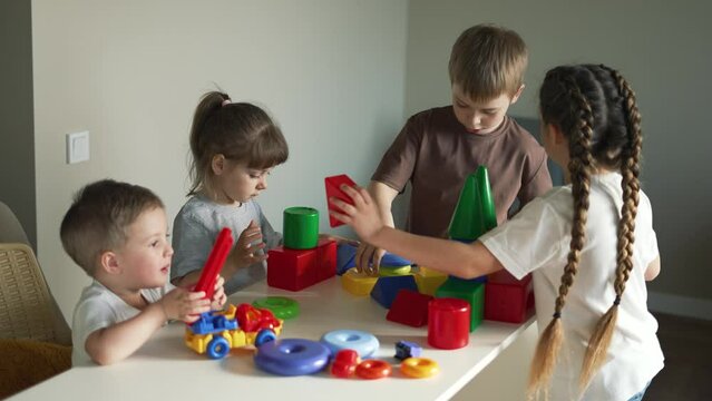 Children in kindergarten. Preschool education in games. Boys and girls play at table at home. Colored cubes and pyramid on table. Child care in kindergarten. Children play and dream. Toy car in hands