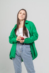 A cute brown-haired girl holds a red ripe apple in her hands on a white background. The model is wearing a green shirt and blue jeans.