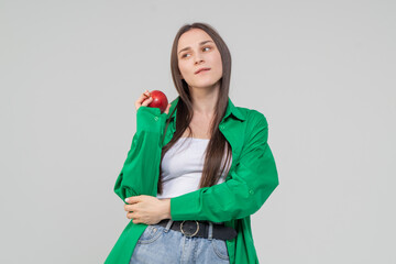 A cute brown-haired girl holds a red ripe apple in her hands on a white background. The model is wearing a green shirt and blue jeans.