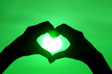 Fototapeta premium Pop art style silhouette of hand making heart sign to the bright sun on vibrant green sky