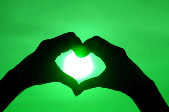Pop art style silhouette of hand making heart sign to the bright sun on vibrant green sky