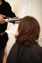 Fototapeta premium 女性の髪にヘアアイロンをかける男性美容師