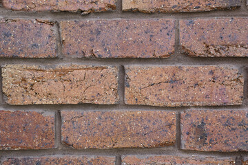 Extreme close-up brownish crimson coloured coarse rustic house bricks with vertical and horizontal joint lines 