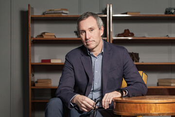 Friendly and confident mature businessman looking at camera and holding glasses