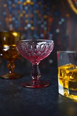 Glamorous, Vintage Pink Chalice Cocktail Glass on a Bar Counter Amidst a Beaded Curtain and a Whirlwind of Cocktails