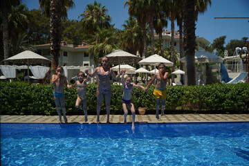 Happy friends jumping in pool on the vacations.