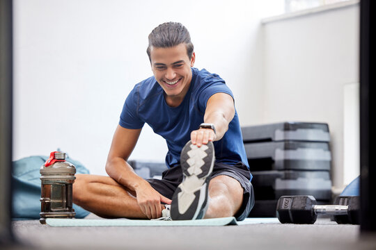 Fitness, gym or man stretching legs starting training, workout or exercise warm up to relax muscles. Wellness, flexible or healthy sports athlete with a happy smile exercising in a studio in Brazil