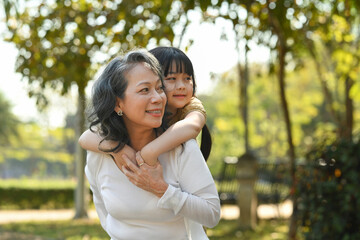 Smiling mature grandmother giving piggyback ride to cute little granddaughter during walking on in...