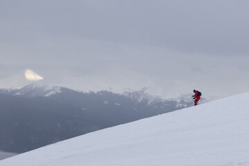 Naklejka na ściany i meble The skier rides high in the snow in the mountains. Fog on the mountain and people skiing