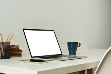 Laptop computer with blank screen, tablet, books and cup of coffee on white table