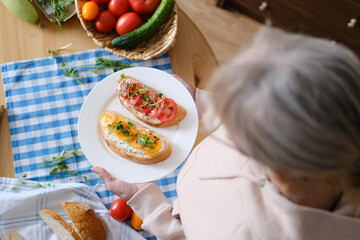 Aged woman holds in her hands a plate with healthy sandwiches with microgreens and vegetables