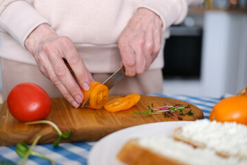Aged woman cuts fresh vegetables for healthy sandwiches