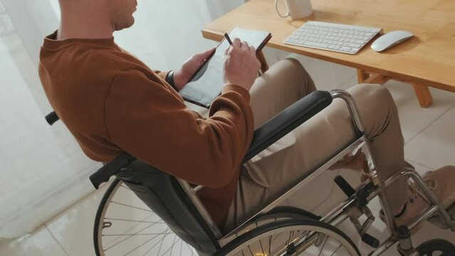 Cropped shot of Caucasian wheelchaired man drawing on graphic tablet while working from home
