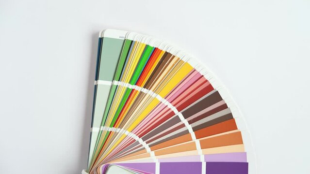 Female Hand opening Color guide close up. Assortment of Colour samples for design. Colors palette fan on white concrete wall background. Graphic designer chooses colors. Coloured swatches catalogue 4K