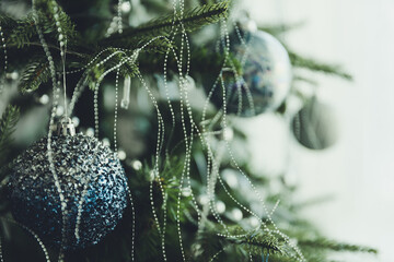 Close up of blue and silver glass toys on Christmas tree with copy space on gray curtains as a...
