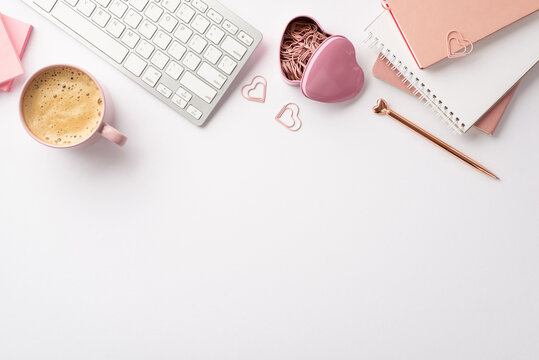 Valentine's Day concept. Top view photo of keyboard notebooks stylish pen heart shaped clips holder and cup of coffee on isolated white background with empty space