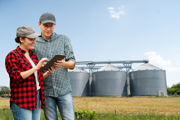 Farmers with digital tablet in front of agricultural silo 