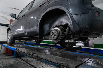 Dirty bottom of car hanging on lift in car workshop. Car service.  Repairing of vehicle brakes. Nobody. Close up from below view of car lifted up for repairs in workshop. Soft focus