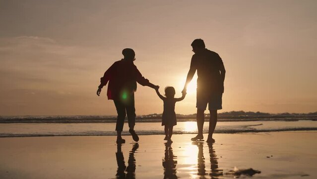 Happy Modern Muslim Southeast Asian Indonesian Family Enjoying Sunset Together on Beach. Silhouette of Father Mother and Child in Slow Motion.