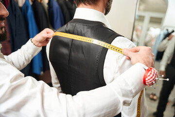 Experienced clothier taking client body measurements in studio
