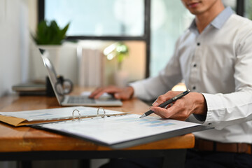 Cropped shot of professional businessman analyzing financial market, using laptop computer at work station