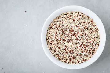 Quinoa. Red white brown quinoa seeds in bowl. Mixed organic raw quinoa seeds on gray stone background.