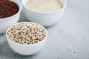Quinoa. Red white brown quinoa seeds in bowl. Mixed raw quinoa seeds on gray stone background.
