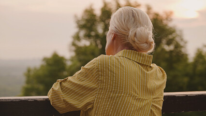 Lonely senior woman standing near fence, looking into distance, missing children