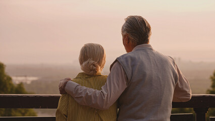 Happy senior couple enjoying sunset view together, loving husband hugging wife