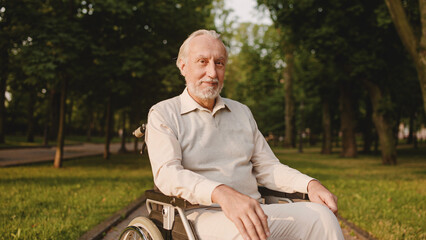 Satisfied man in wheelchair smiling at camera, resting in park, nursing home