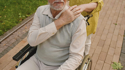 Retired man with disability stroking wife's hand outdoors, happy family