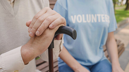 Volunteer supporting aged person with disability, sitting on bench with man with disability