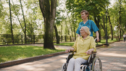 Fototapeta premium Female nurse pushing wheelchair with senior woman patient, nursing home services, health